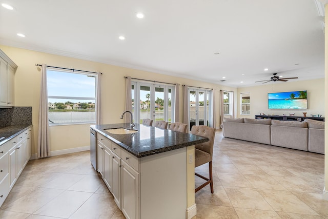 kitchen with french doors, sink, a breakfast bar area, an island with sink, and dark stone counters