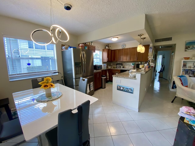 kitchen featuring pendant lighting, stainless steel fridge, light stone countertops, a textured ceiling, and decorative backsplash