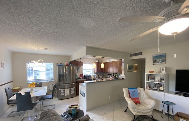 living area featuring ceiling fan with notable chandelier, a textured ceiling, light tile patterned flooring, and visible vents