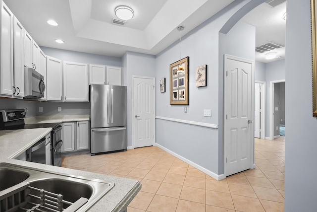 kitchen featuring white cabinets, stainless steel appliances, a tray ceiling, and light tile patterned floors