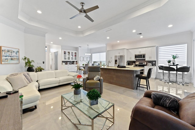 living room featuring crown molding, ceiling fan, a tray ceiling, and sink