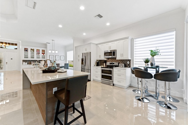 kitchen with a kitchen bar, white cabinetry, a center island with sink, pendant lighting, and stainless steel appliances