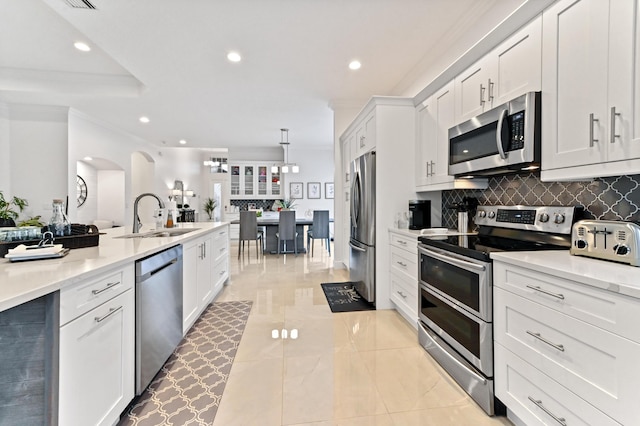 kitchen with sink, white cabinetry, backsplash, stainless steel appliances, and ornamental molding