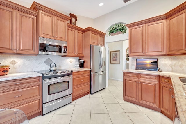 kitchen featuring light tile patterned flooring, appliances with stainless steel finishes, light stone counters, and backsplash