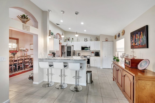 kitchen featuring a kitchen bar, stainless steel appliances, a peninsula, light tile patterned floors, and vaulted ceiling