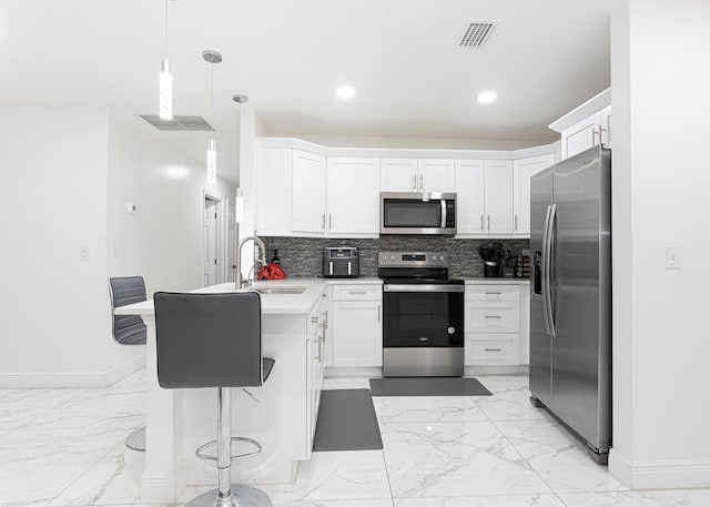 kitchen with appliances with stainless steel finishes, white cabinets, a kitchen breakfast bar, and decorative light fixtures