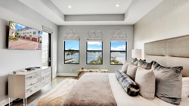 bedroom with a water view, a tray ceiling, light hardwood / wood-style floors, and multiple windows