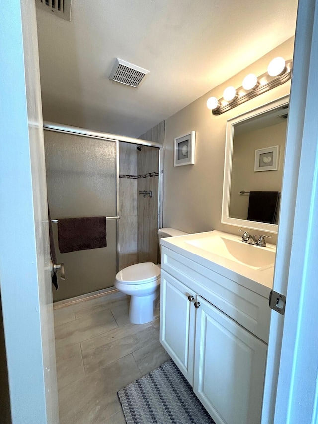 bathroom featuring a shower with door, vanity, and toilet