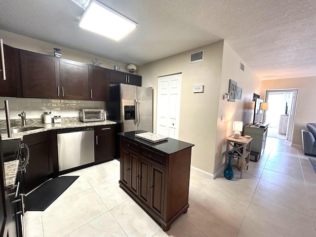 kitchen featuring sink, backsplash, stainless steel appliances, dark brown cabinetry, and a kitchen island