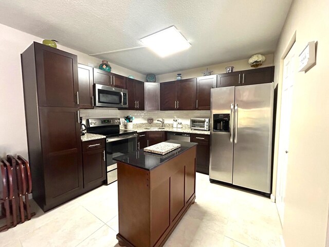 kitchen featuring dark brown cabinetry, decorative backsplash, a kitchen island, and appliances with stainless steel finishes