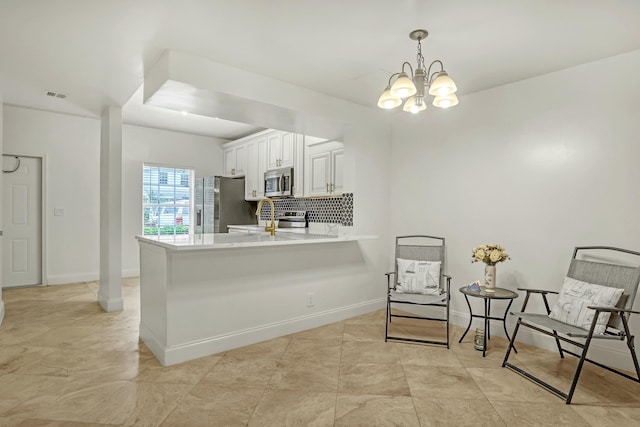 kitchen with white cabinetry, decorative light fixtures, appliances with stainless steel finishes, kitchen peninsula, and backsplash