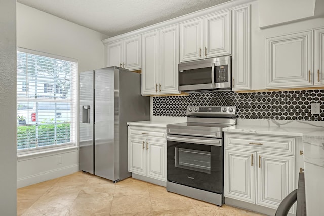 kitchen with light tile patterned flooring, white cabinetry, light stone counters, stainless steel appliances, and backsplash