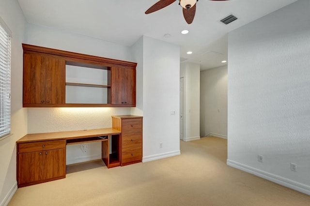 unfurnished office with ceiling fan, built in desk, and light carpet