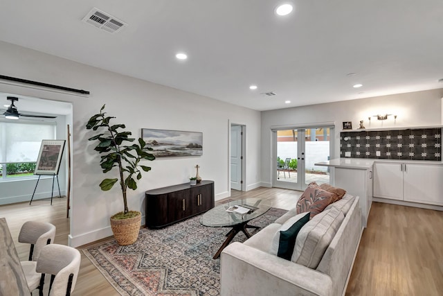 living room featuring a barn door, plenty of natural light, light wood-type flooring, and french doors