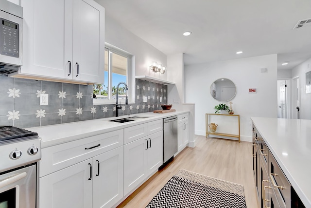 kitchen with sink, tasteful backsplash, light hardwood / wood-style flooring, appliances with stainless steel finishes, and white cabinets