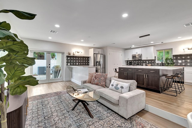 living room with french doors, sink, and light hardwood / wood-style floors