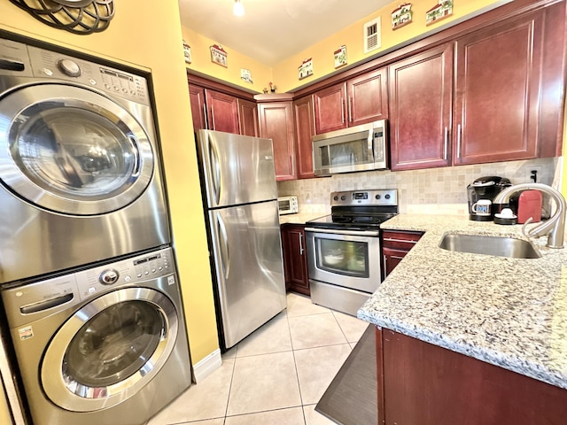 kitchen featuring sink, light tile patterned floors, stacked washing maching and dryer, appliances with stainless steel finishes, and light stone counters