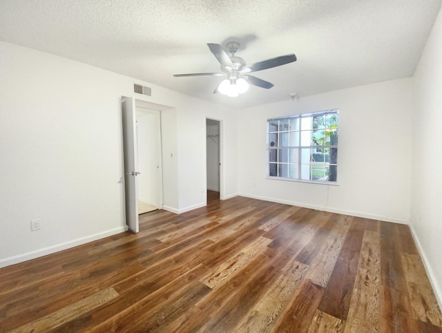 unfurnished bedroom with a spacious closet, ceiling fan, dark wood-type flooring, a textured ceiling, and a closet