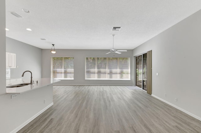 unfurnished living room with ceiling fan, sink, hardwood / wood-style floors, and a textured ceiling