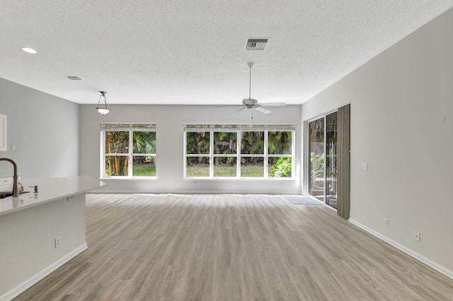 unfurnished living room with ceiling fan, sink, a textured ceiling, and light wood-type flooring