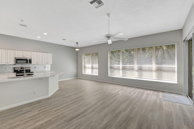 kitchen with light hardwood / wood-style flooring, appliances with stainless steel finishes, white cabinetry, decorative backsplash, and decorative light fixtures