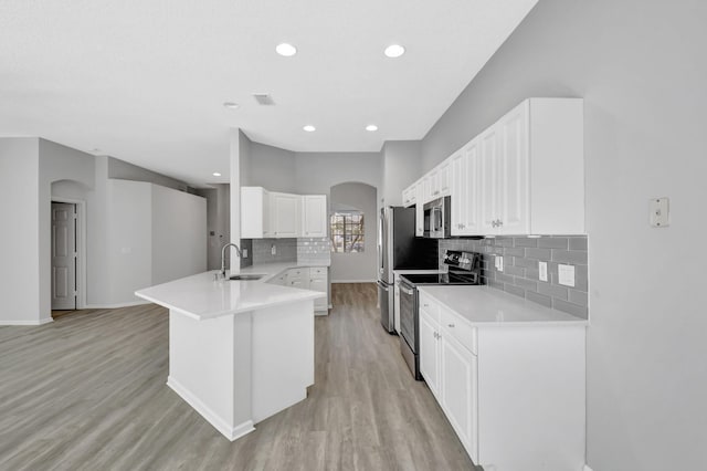 kitchen with sink, appliances with stainless steel finishes, white cabinetry, kitchen peninsula, and light wood-type flooring