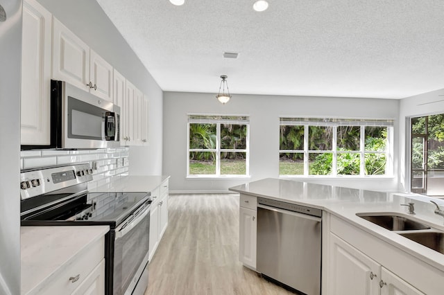 kitchen featuring stainless steel appliances, a healthy amount of sunlight, white cabinets, and decorative light fixtures