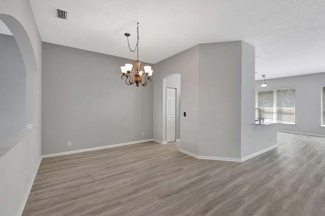 unfurnished room with a textured ceiling, light hardwood / wood-style flooring, and a chandelier