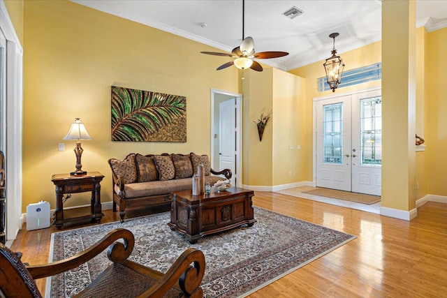 living room featuring french doors, ornamental molding, ceiling fan with notable chandelier, and light hardwood / wood-style floors