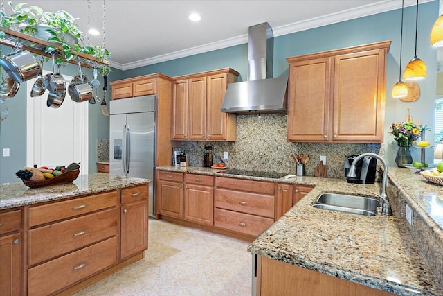 kitchen with pendant lighting, sink, light stone counters, built in fridge, and wall chimney exhaust hood