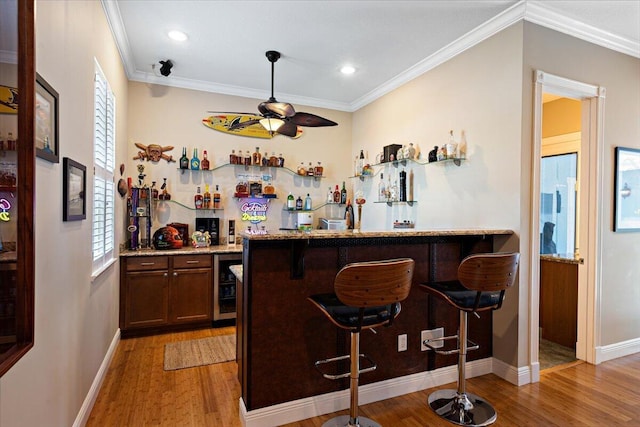 bar with light stone countertops, ornamental molding, light hardwood / wood-style floors, and beverage cooler