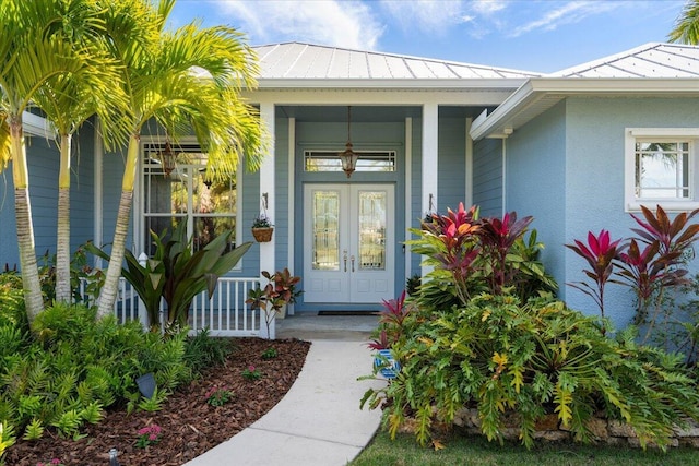 property entrance with stucco siding, a standing seam roof, french doors, covered porch, and metal roof