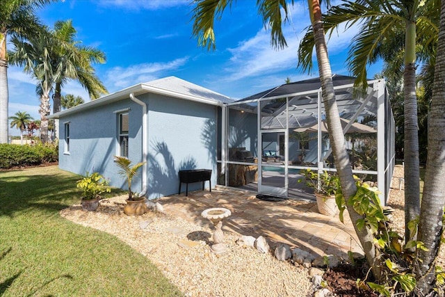 view of home's exterior with glass enclosure, a patio, a lawn, and stucco siding