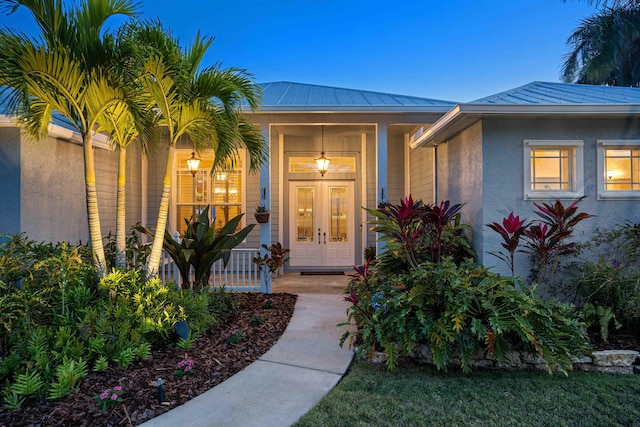 property entrance featuring a standing seam roof, covered porch, stucco siding, french doors, and metal roof