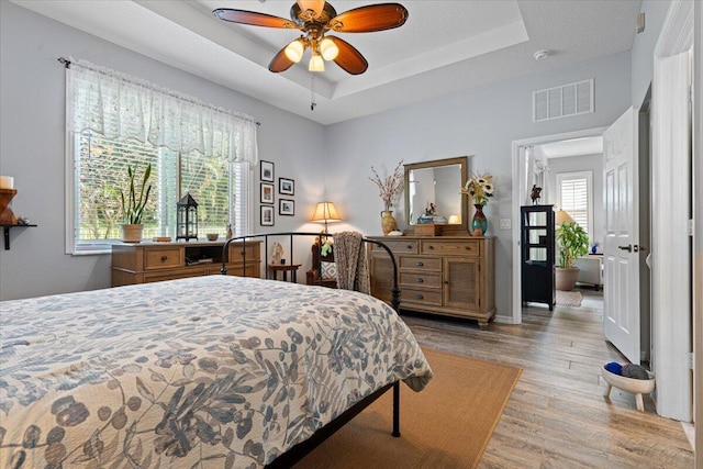 bedroom featuring a raised ceiling, ceiling fan, and light wood-type flooring