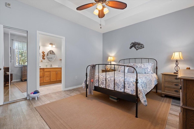 bedroom featuring a raised ceiling, connected bathroom, and light hardwood / wood-style flooring