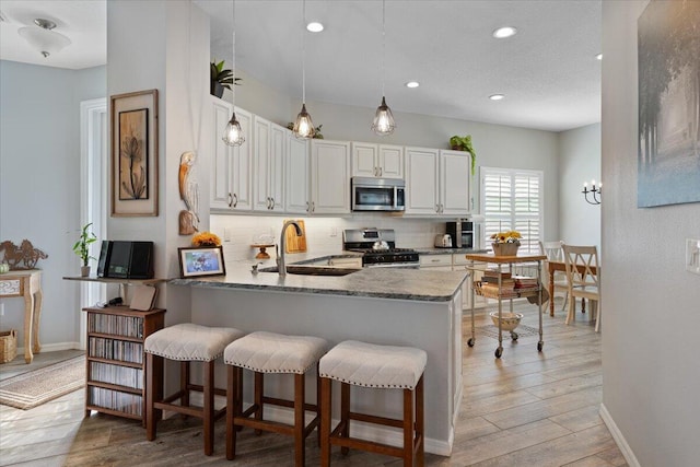 kitchen with sink, tasteful backsplash, kitchen peninsula, stainless steel appliances, and white cabinets