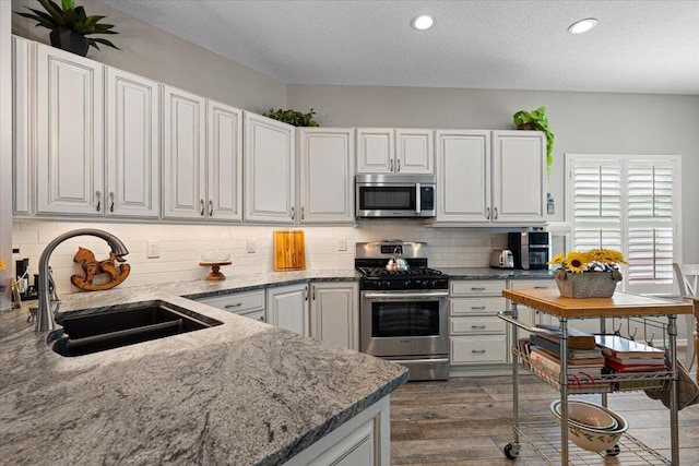 kitchen featuring sink, white cabinetry, backsplash, stainless steel appliances, and light stone counters