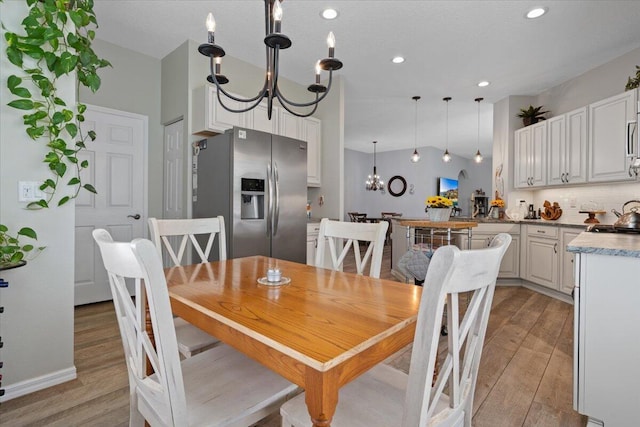 dining space with vaulted ceiling, sink, light hardwood / wood-style floors, and a notable chandelier