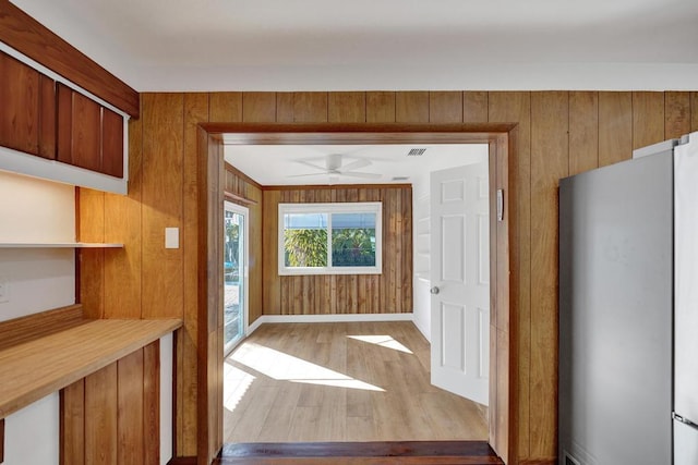 interior space with ceiling fan, wooden walls, and light wood-type flooring