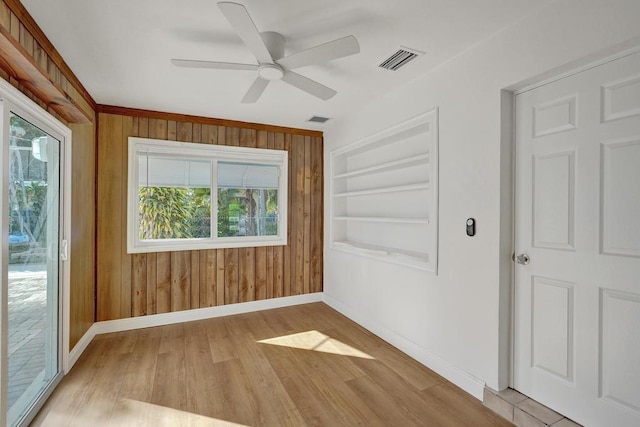 empty room with a healthy amount of sunlight, wood walls, light wood-type flooring, and built in shelves