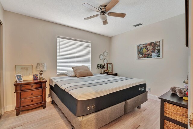 bedroom with light wood-type flooring, ceiling fan, a textured ceiling, and a closet