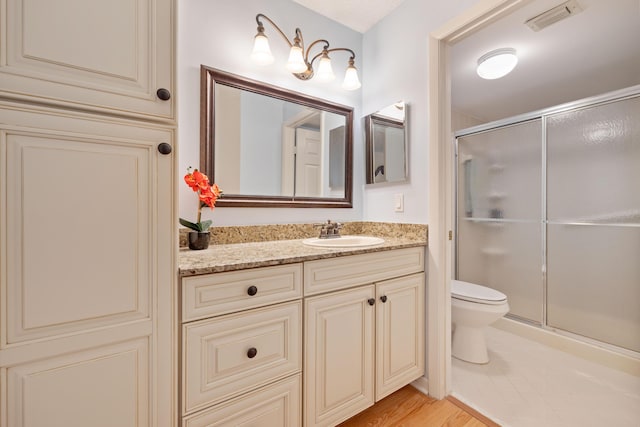 bathroom with hardwood / wood-style flooring, vanity, an enclosed shower, and toilet