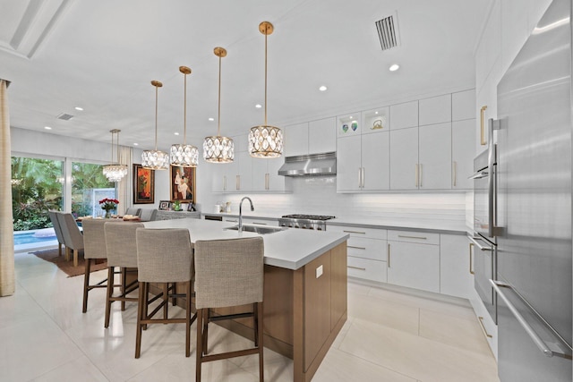 kitchen featuring decorative light fixtures, sink, white cabinets, stainless steel appliances, and a center island with sink