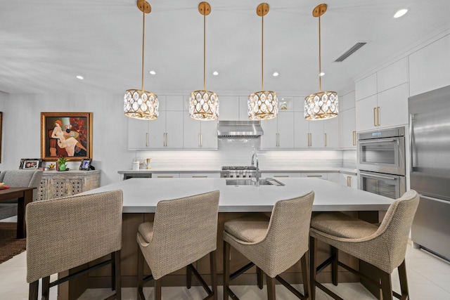 kitchen with sink, appliances with stainless steel finishes, a kitchen island with sink, decorative backsplash, and decorative light fixtures