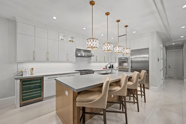 kitchen featuring appliances with stainless steel finishes, sink, wine cooler, hanging light fixtures, and a kitchen island with sink