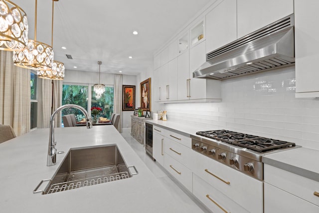 kitchen with pendant lighting, ventilation hood, white cabinetry, sink, and stainless steel gas cooktop