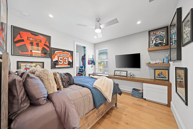 bedroom with built in desk, a closet, a walk in closet, ceiling fan, and light hardwood / wood-style flooring