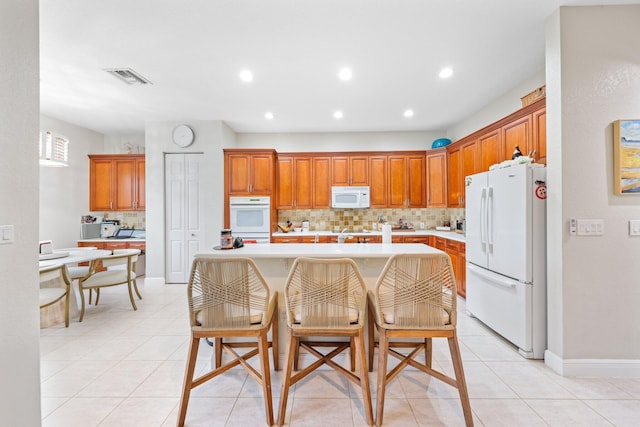 kitchen with light tile patterned flooring, a kitchen island, a kitchen breakfast bar, decorative backsplash, and white appliances