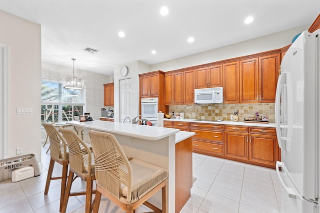 kitchen featuring tasteful backsplash, decorative light fixtures, a kitchen breakfast bar, white appliances, and a kitchen island with sink